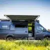 Seitenansicht eines ausgebauten Mercedes Sprinter 170 2500 4x4 Campervans mit ausgefahrener Markise auf einer Wiese