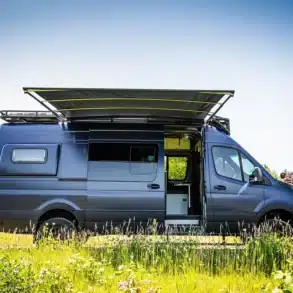 Seitenansicht eines ausgebauten Mercedes Sprinter 170 2500 4x4 Campervans mit ausgefahrener Markise auf einer Wiese