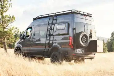 Schwarzer Mercedes Sprinter 4x4 Campervan mit Dachträger, Leiter und Reserverad im offenen Gelände