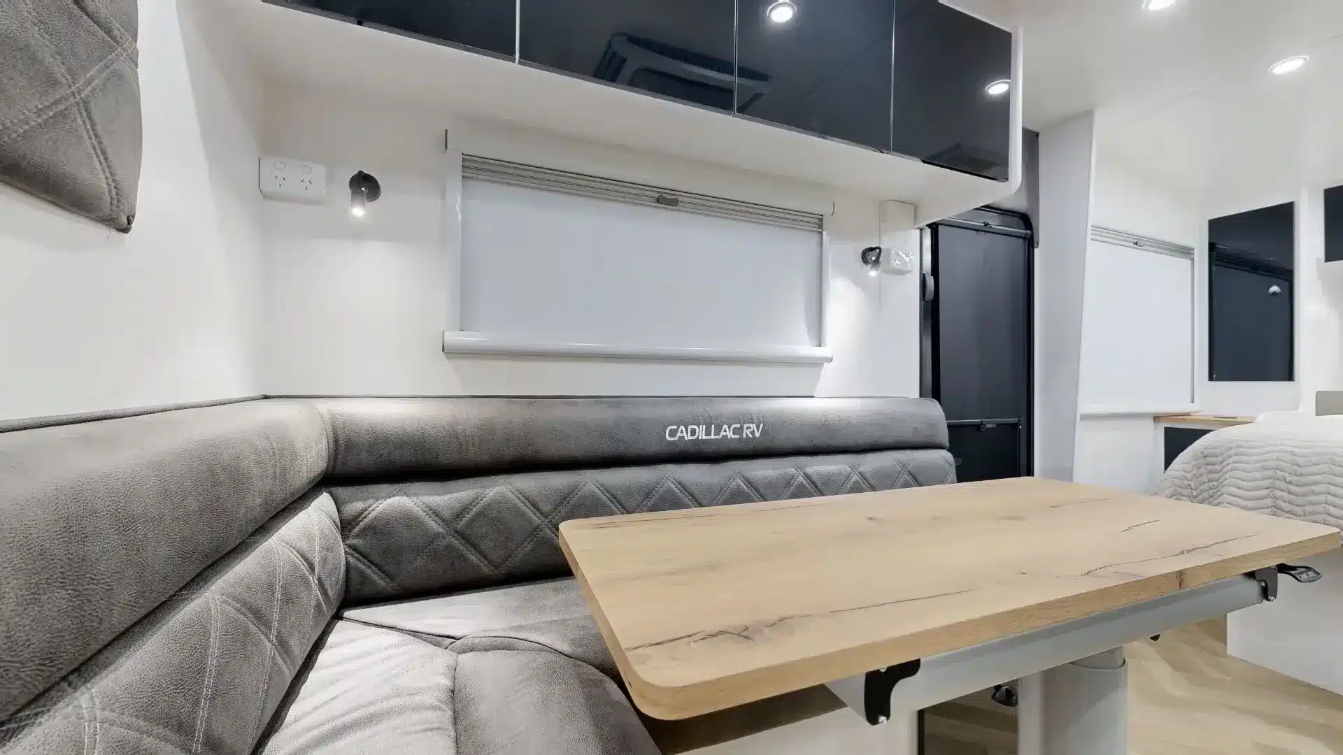 L‑förmige Lounge mit grauer Polsterung und Holztisch im Innenraum des Cadillac RV 216 Gaia