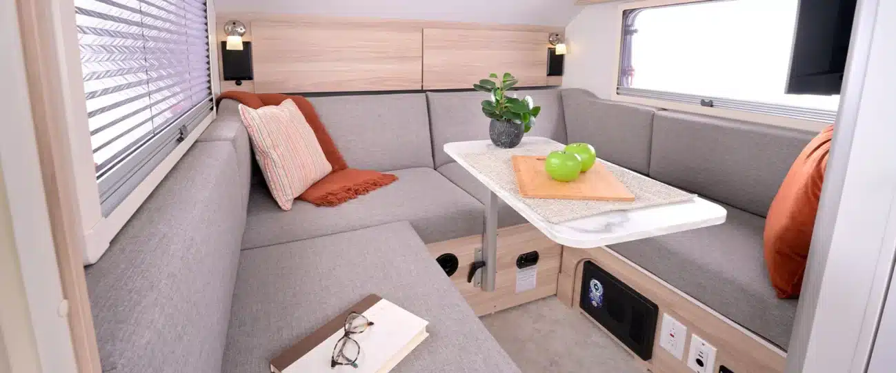Innenansicht des TAB 320 LITE Campers mit grauer Polster-Sitzgruppe, Tisch, Kissen und Fenster