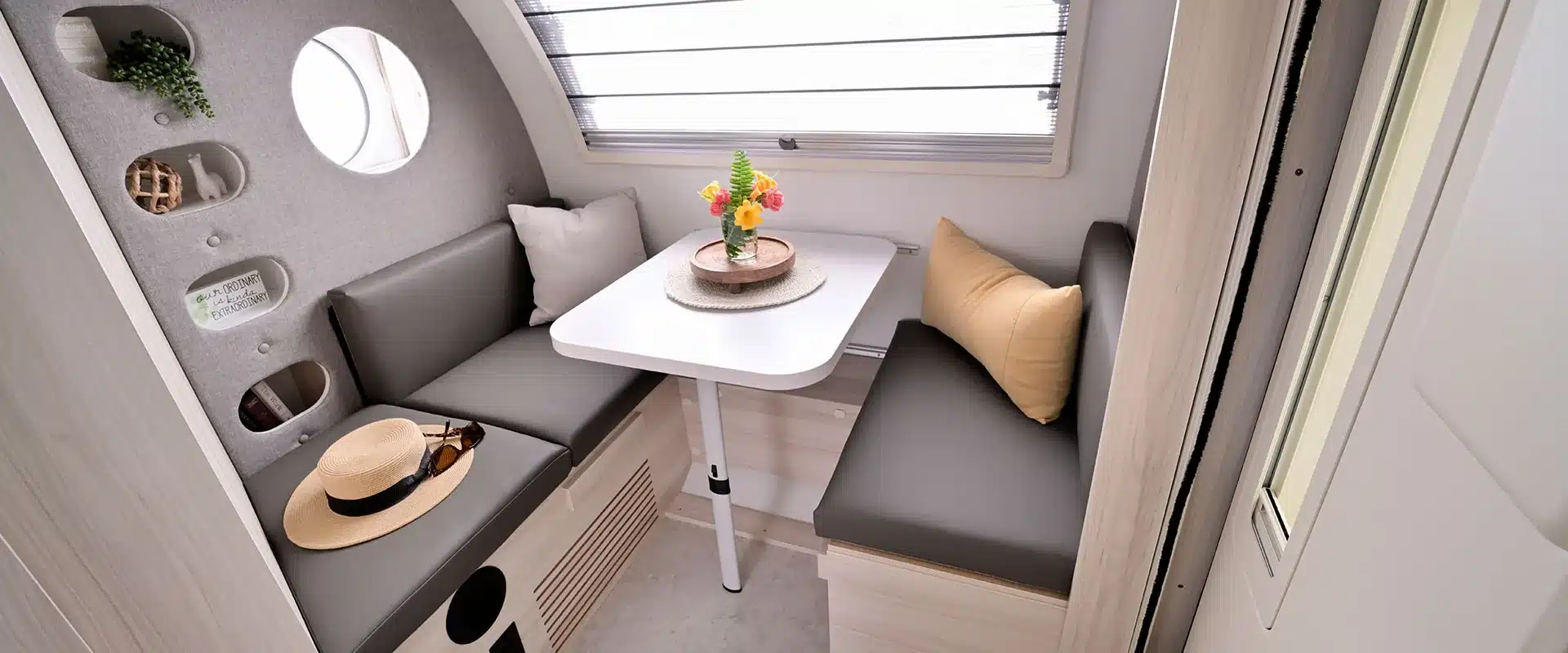 Dinette-Bereich mit grauen Polstern, weißem Tisch und runden Regalfächern im Innenraum eines TAB 400 Teardrop Campers