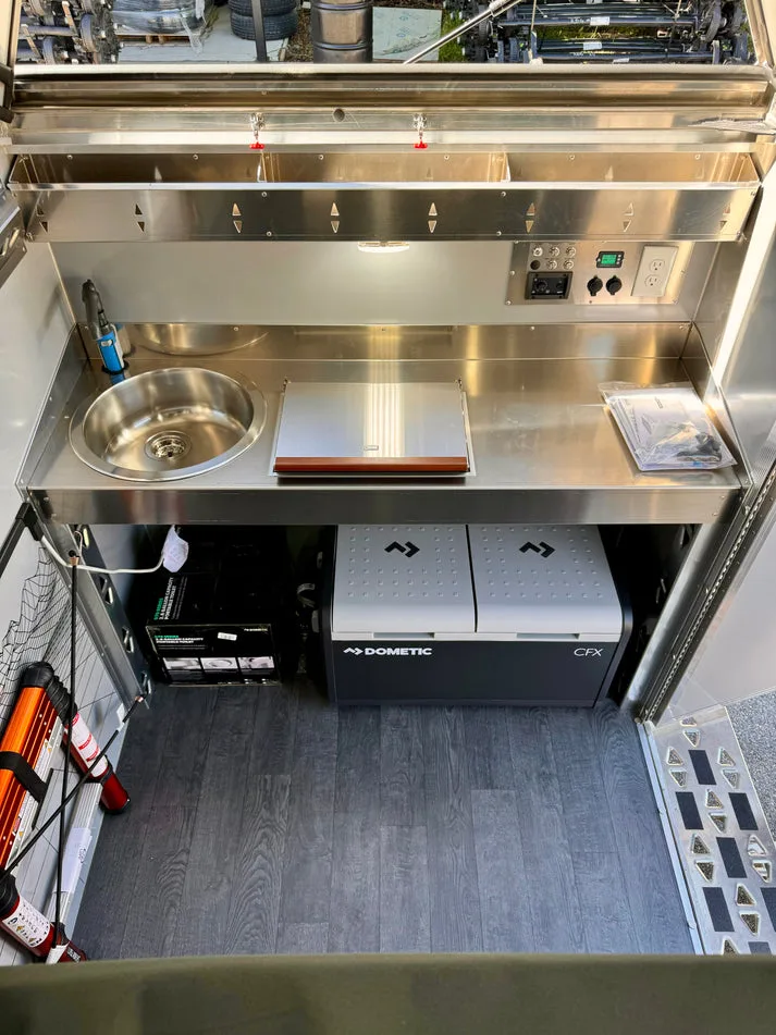 Innenansicht des AntiShanty AS-1 A-Frame Trailers mit Edelstahl-Küchenmodul, Spüle, Arbeitsfläche, Dometic-Kühlbox und Stauraum