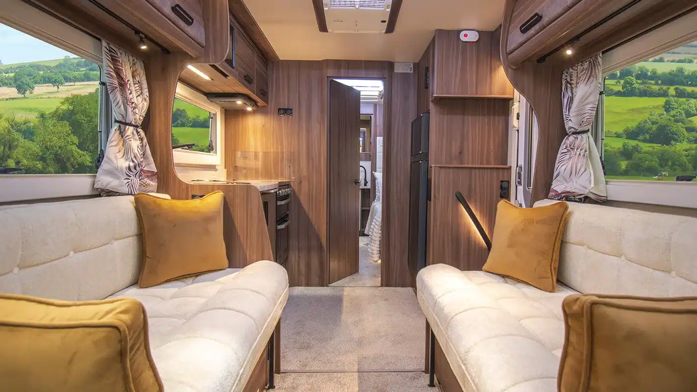 Wohnbereich des Auto-Sleepers Burford Duo mit zwei Sofas, Holzmöbeln und Blick in die Küche