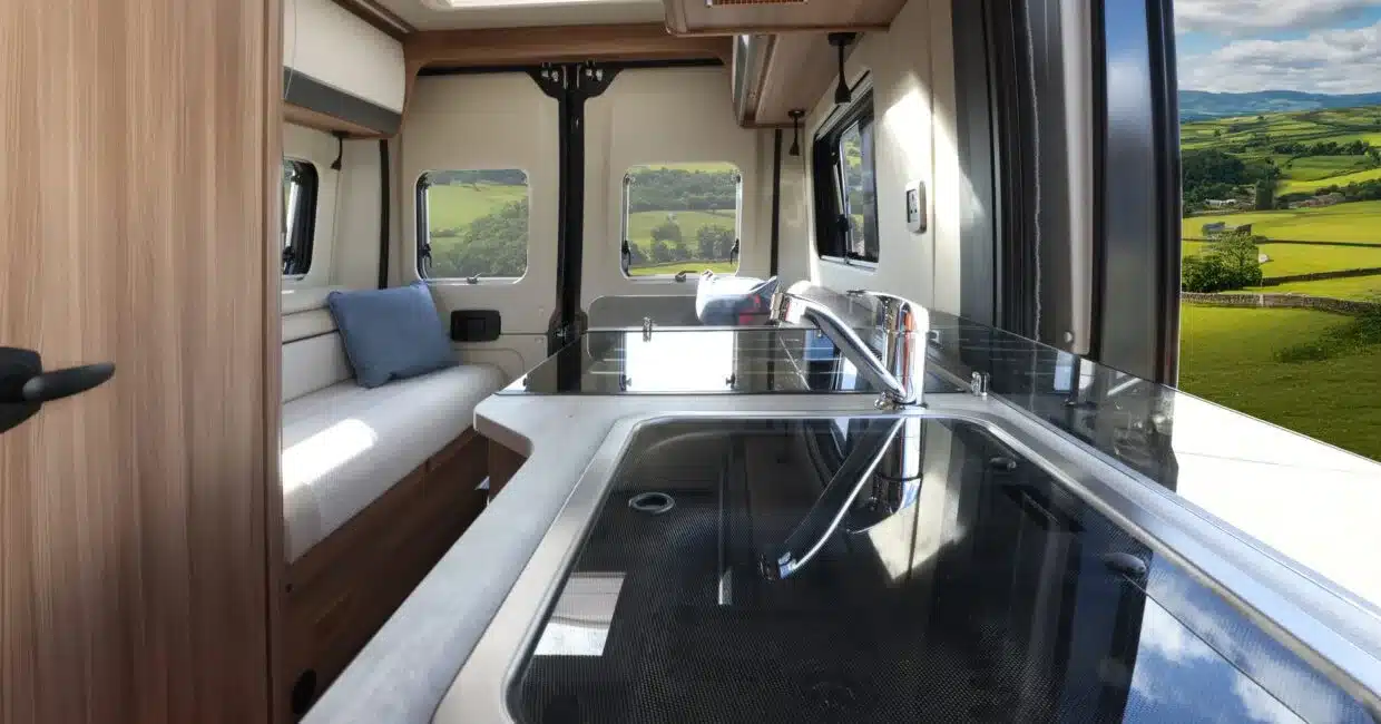 Blick in den Innenraum eines Auto-Trail V-Line 540 SE Kastenwagens mit Küchenzeile, Sofa und Fenstern mit Blick in die grüne Landschaft