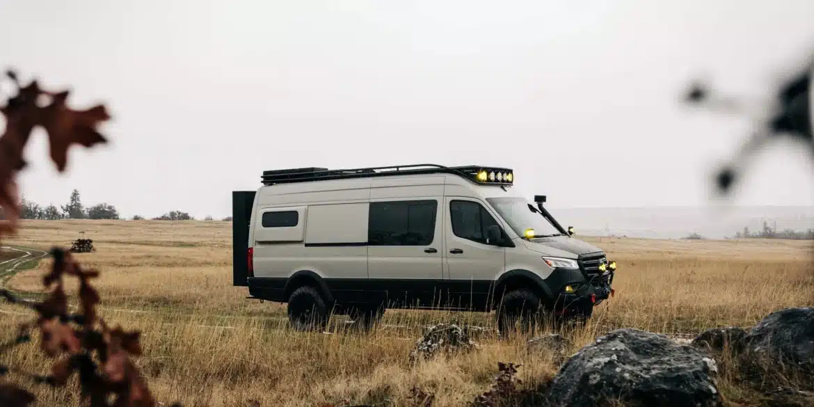 AWOL Sprinter Iglhaut Allrad 170 auf einer Wiese im Gelände, ausgestattet mit Dachträger, Zusatzscheinwerfern und Offroad-Bereifung