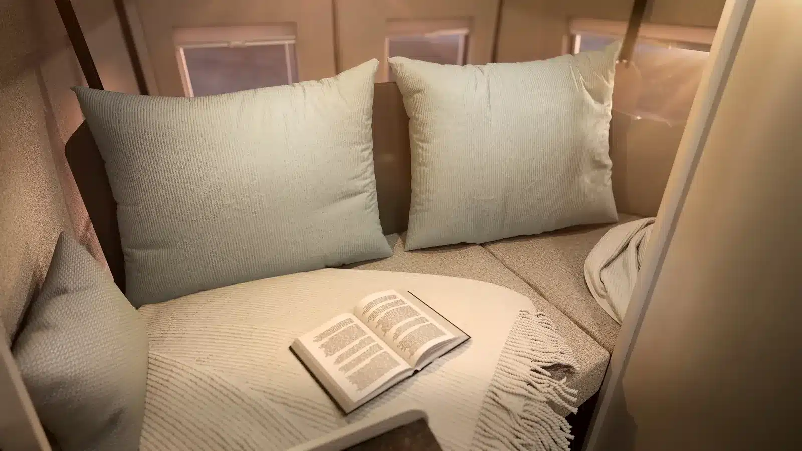Innenraum des Bürstner Papillon mit umgebauter Sitz- und Schlaflandschaft, Kissen und aufgeschlagenem Buch