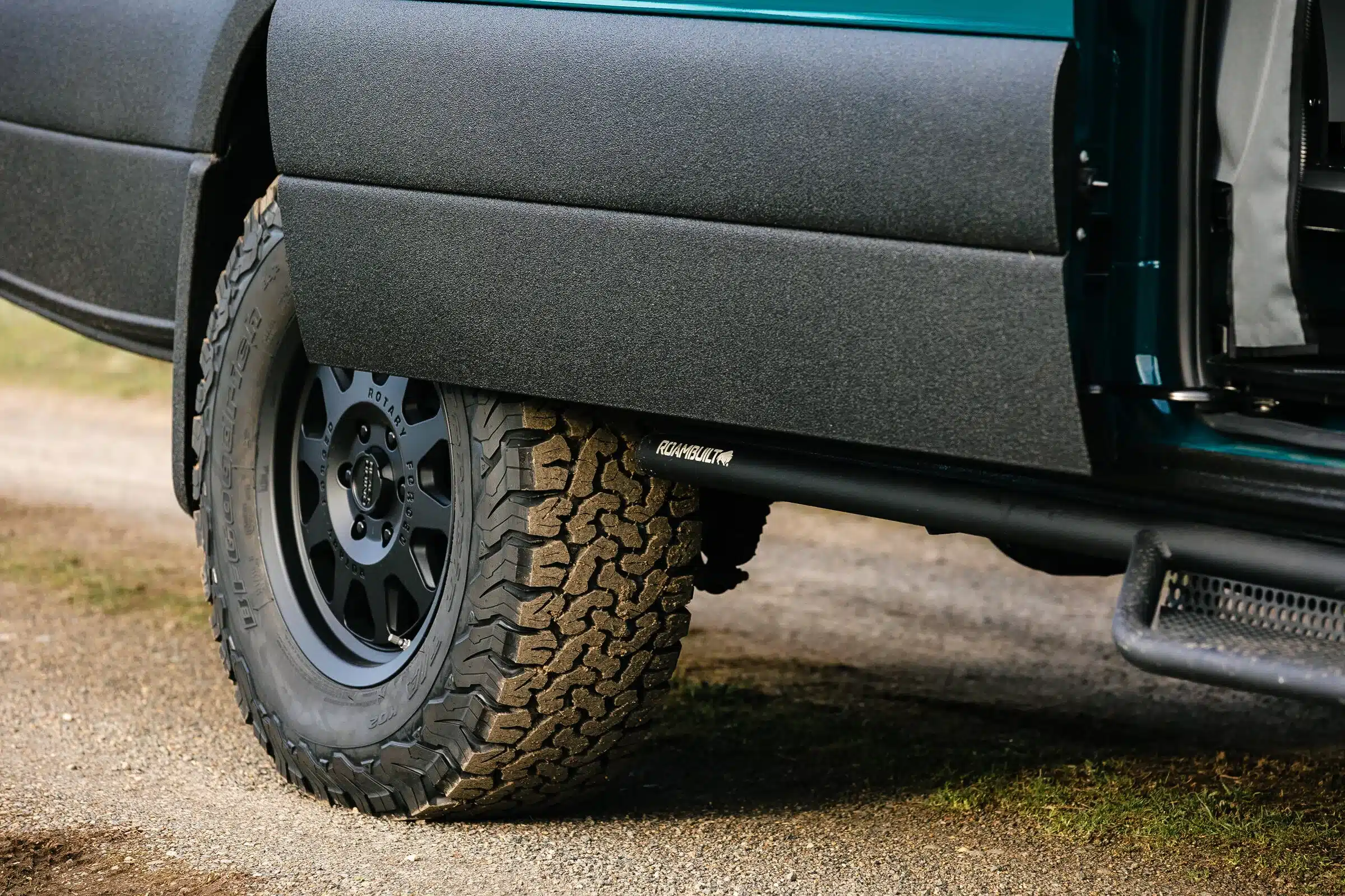 Nahaufnahme eines Offroad-Reifens mit Felge, Line-X-beschichtetem Schweller und Trittstufe am Benchmark Acorn 4x4 Sprinter