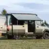 Benchmark Apprentice Campervan auf Mercedes Sprinter 144 AWD Basis mit ausgefahrener Markise auf einer Wiese