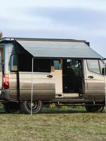 Benchmark Apprentice Campervan auf Mercedes Sprinter 144 AWD Basis mit ausgefahrener Markise auf einer Wiese