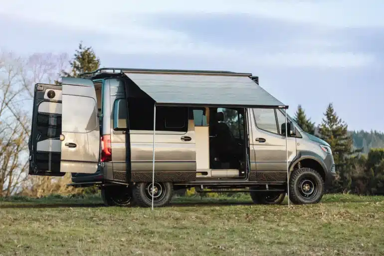 Benchmark Apprentice Campervan auf Mercedes Sprinter 144 AWD Basis mit ausgefahrener Markise auf einer Wiese