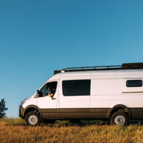 Seitenansicht eines weißen Mercedes Sprinter 170 4x4 Benchmark b wagon Campervans auf einer Wiese unter blauem Himmel