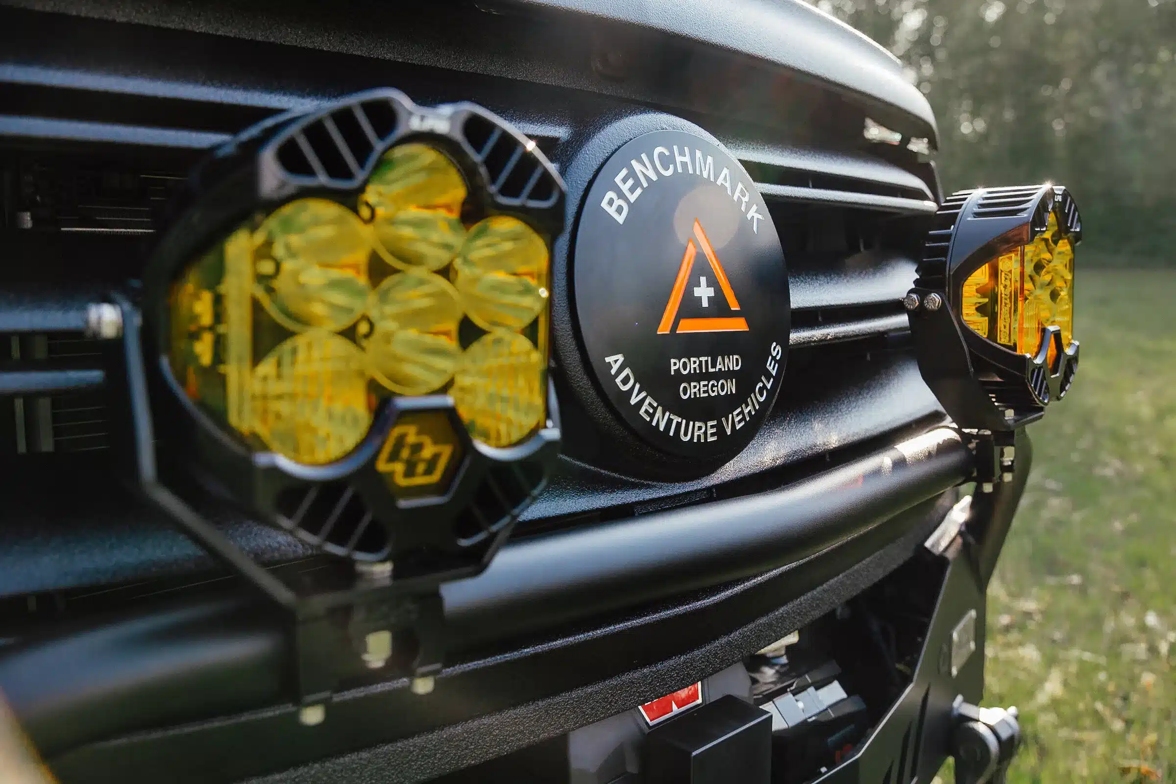 Nahaufnahme des Kühlergrills eines Benchmark Adventure Vehicles CUBMOBILE mit gelben Offroad-Zusatzscheinwerfern und Herstellerlogo