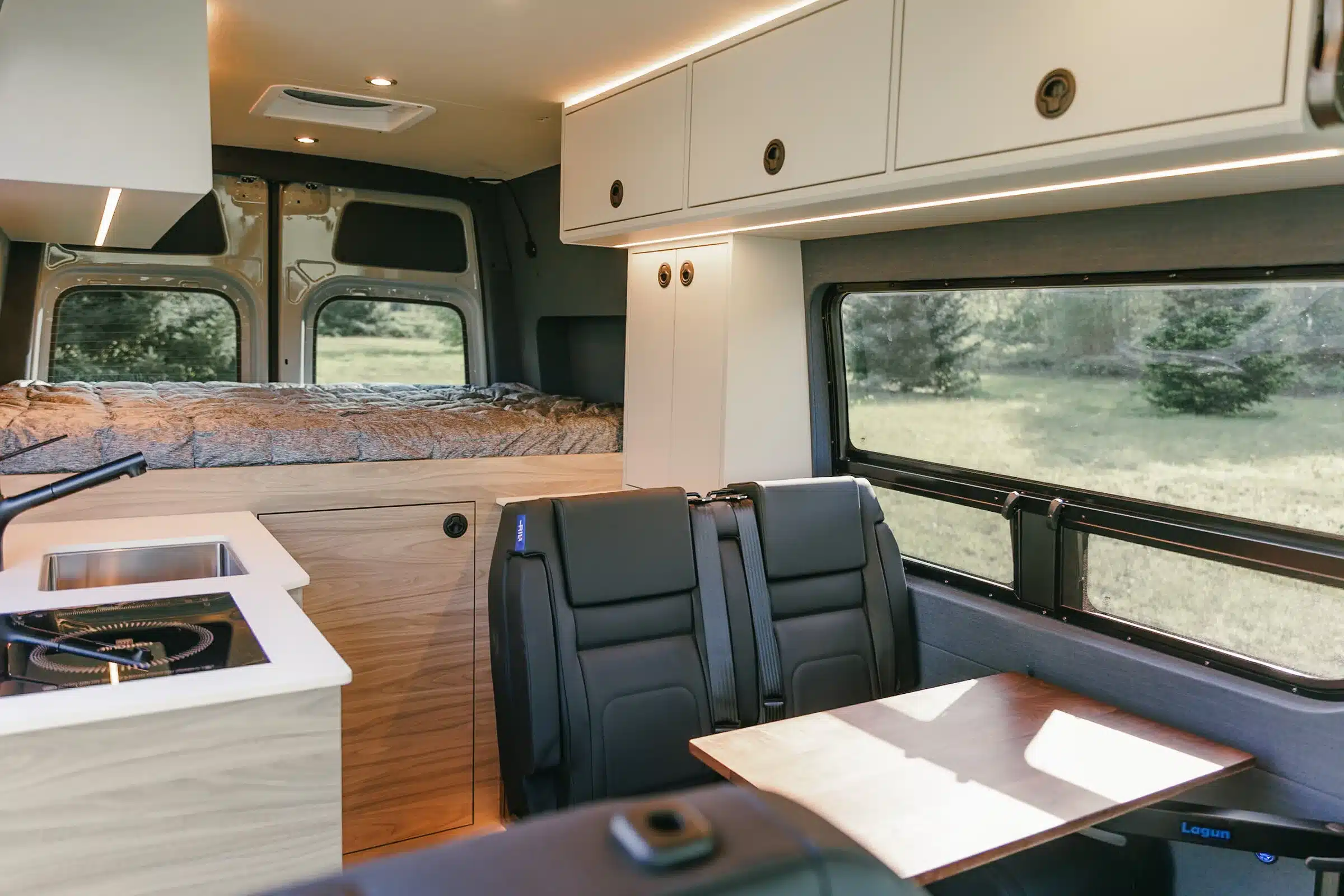 Innenansicht eines ausgebauten Mercedes Sprinter Benchmark CUBMOBILE mit Küchenzeile, Sitzbank, Tisch und Bett im Heck