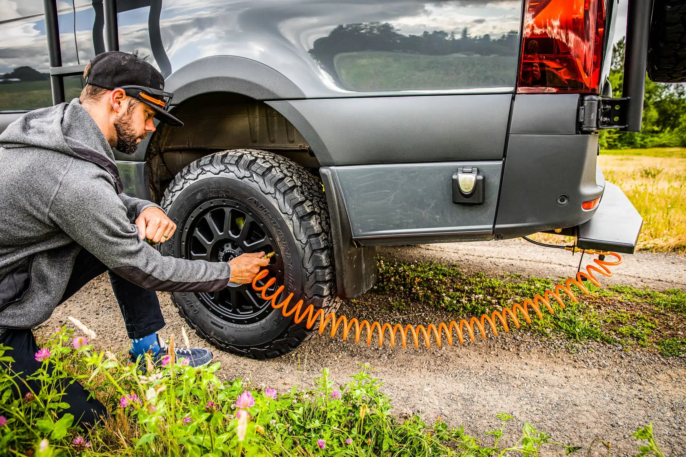 Mann passt den Reifendruck eines Benchmark Elkat Offroad-Campervans mit einem Kompressor an