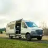 Benchmark Iris Campervan, ausgebauter Mercedes Sprinter 170 4x4 EXT, steht mit geöffneter Schiebetür auf einer Wiese