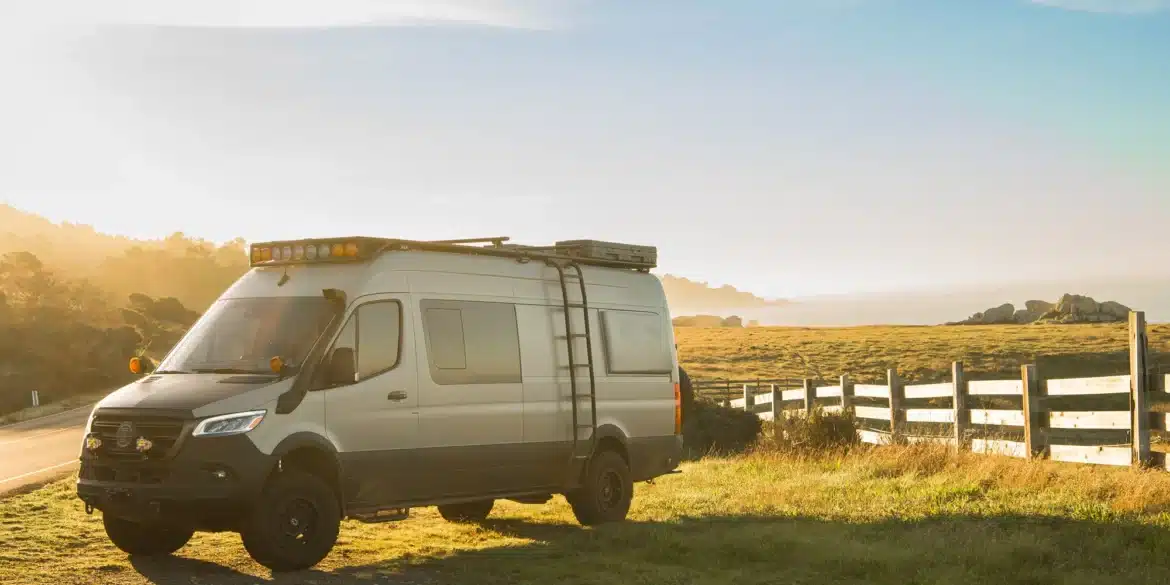 Benchmark Mojave Sprinter 4x4 Expeditionsvan mit Dachträger und Offroad-Ausstattung auf einer Wiese bei Sonnenaufgang