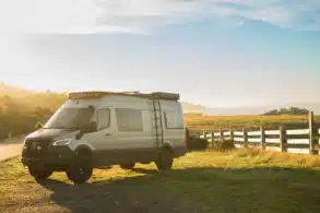 Benchmark Mojave Sprinter 4x4 Expeditionsvan mit Dachträger und Offroad-Ausstattung auf einer Wiese bei Sonnenaufgang