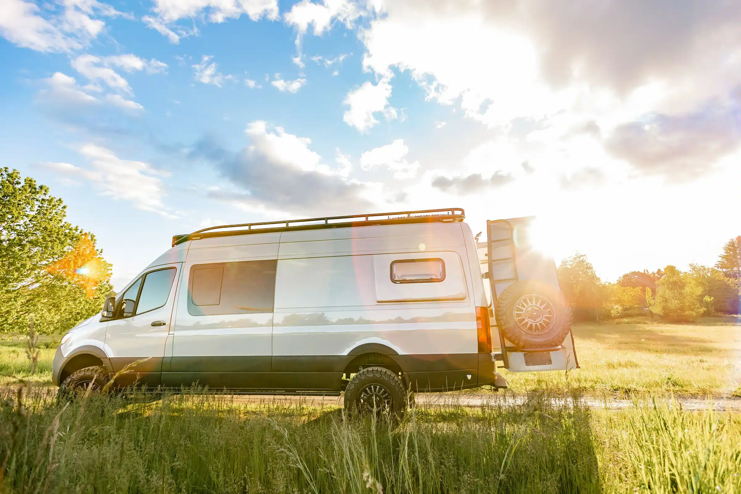 Seitenansicht eines ausgebauten Mercedes Sprinter 170 4x4 Campervans auf einer Wiese bei Sonnenuntergang