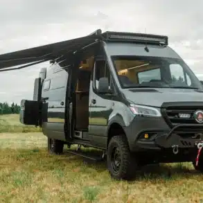 Benchmark Paradise Campervan auf Mercedes Sprinter 170 AWD mit ausgefahrener Markise auf einer Wiese