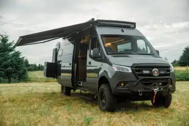 Benchmark Paradise Campervan auf Mercedes Sprinter 170 AWD mit ausgefahrener Markise auf einer Wiese