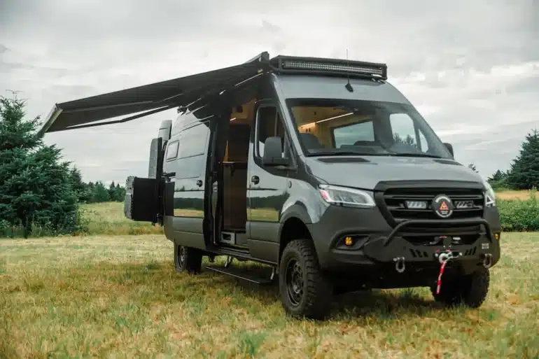 Benchmark Paradise Campervan auf Mercedes Sprinter 170 AWD mit ausgefahrener Markise auf einer Wiese