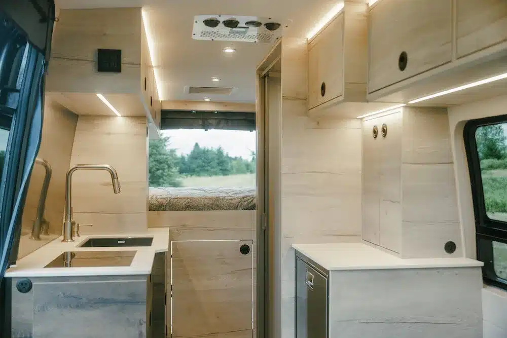 Hochwertig ausgebauter Innenraum eines Benchmark Paradise Vans mit Küchenzeile, Stauraum und Bett