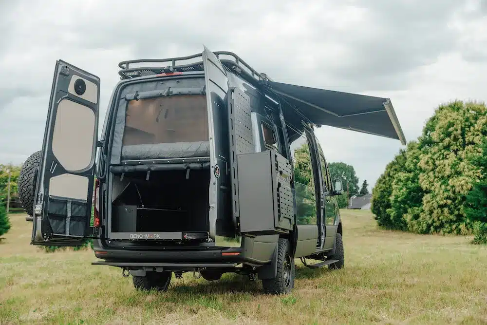Heckansicht des Benchmark Paradise Vans mit geöffneten Türen, Stauraum und Markise auf einer Wiese