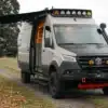 Benchmark Revive Sprinter 2024 Campervan mit Offroad-Ausstattung, Markise und geöffneter Seitentür auf Feldweg