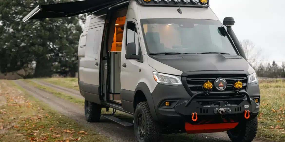Benchmark Revive Sprinter 2024 Campervan mit Offroad-Ausstattung, Markise und geöffneter Seitentür auf Feldweg