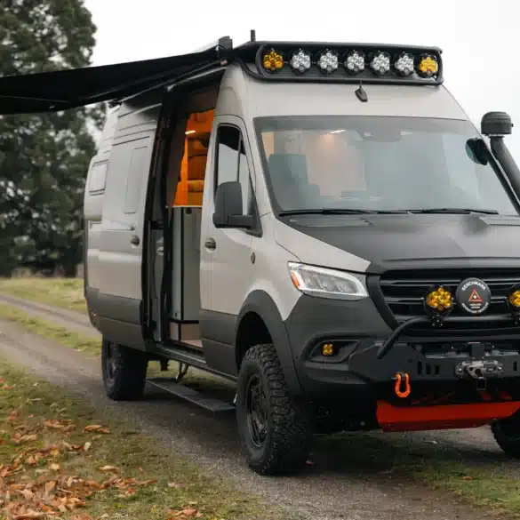Benchmark Revive Sprinter 2024 Campervan mit Offroad-Ausstattung, Markise und geöffneter Seitentür auf Feldweg