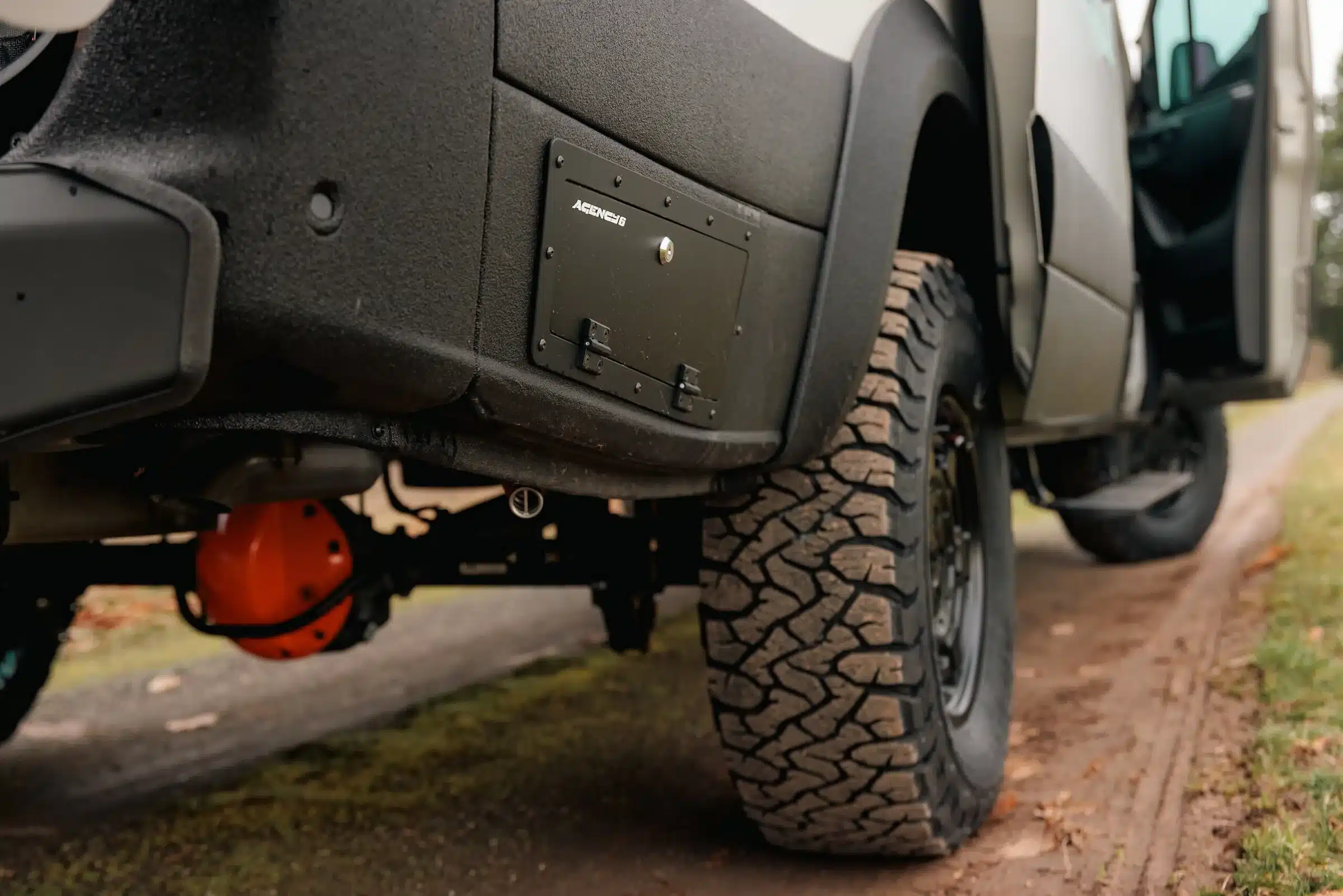 Nahaufnahme des Offroad-Fahrwerks und Unterbodenschutzes eines Benchmark Revive Sprinter Vans mit grobstolligen Reifen auf unbefestigtem Weg