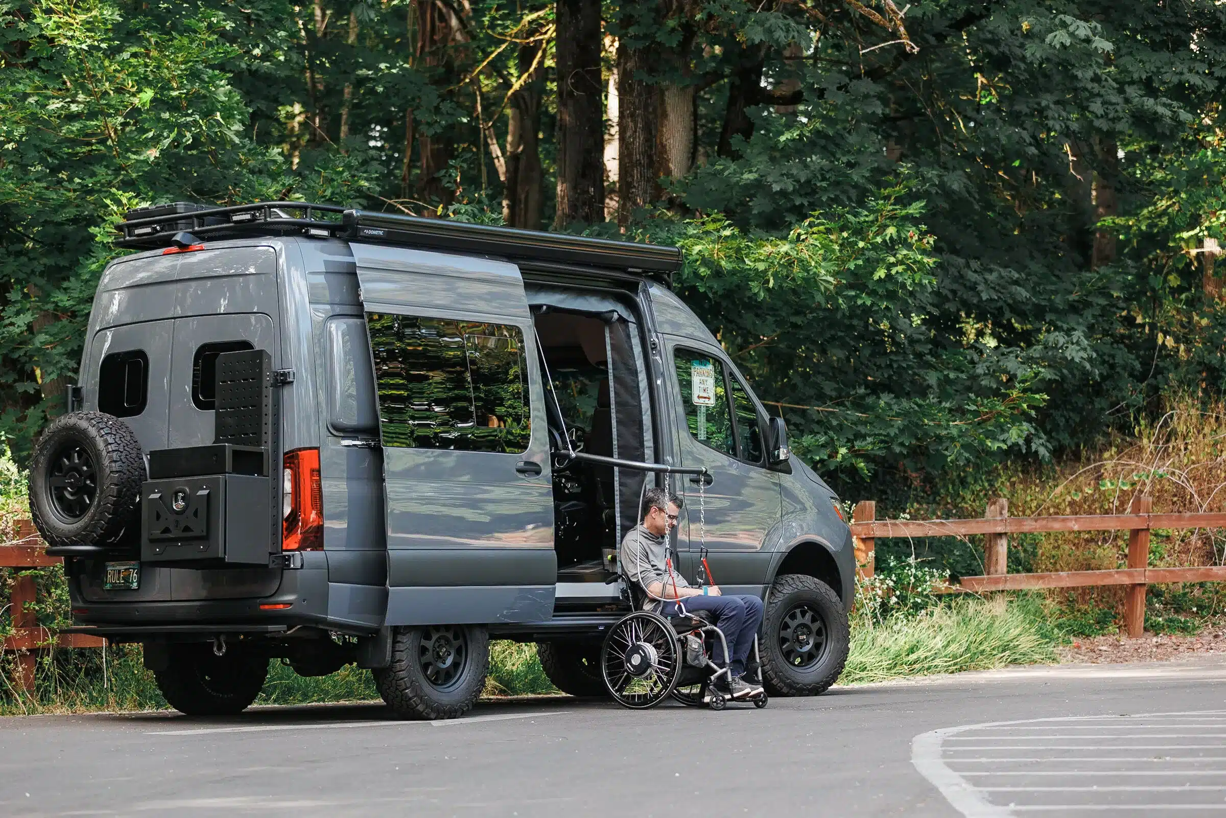 Benchmark Rule 76 Adventure Van mit Rollstuhlfahrer und barrierefreiem Zugang auf einem Parkplatz vor Waldkulisse