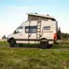 Seitenansicht eines beigen Mercedes Sprinter 144 4x4 Campervans mit Aufstelldach und Leiter, geparkt auf einem Feldweg