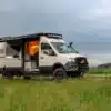 Ausgebauter Benchmark Vehicles Cortland Campervan mit Markise, geöffneten Türen und Offroad-Ausstattung auf einer grünen Wiese