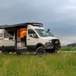 Ausgebauter Benchmark Vehicles Cortland Campervan mit Markise, geöffneten Türen und Offroad-Ausstattung auf einer grünen Wiese