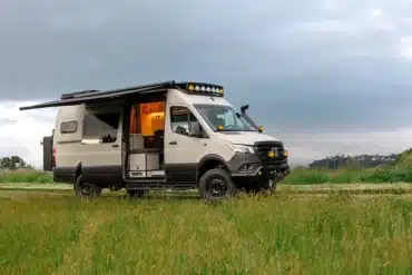 Ausgebauter Benchmark Vehicles Cortland Campervan mit Markise, geöffneten Türen und Offroad-Ausstattung auf einer grünen Wiese