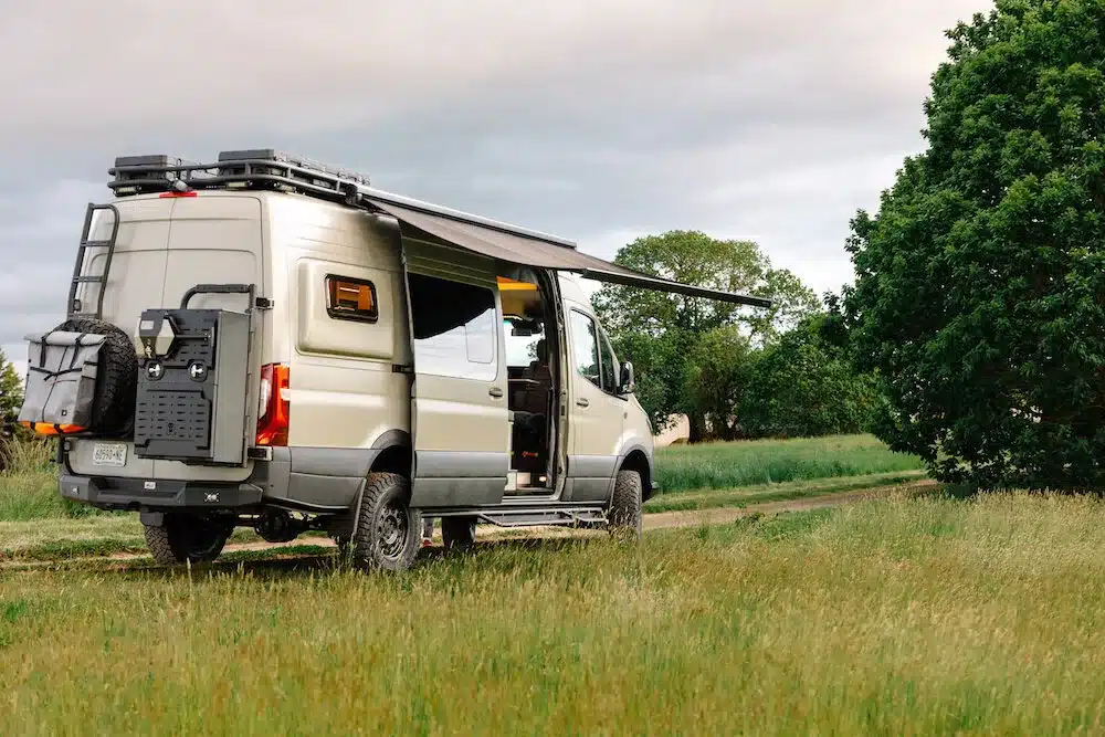 Ausgebauter Benchmark Vehicles Cortland Campervan mit Markise auf einer Wiese, bereit für Offroad und längere Reisen