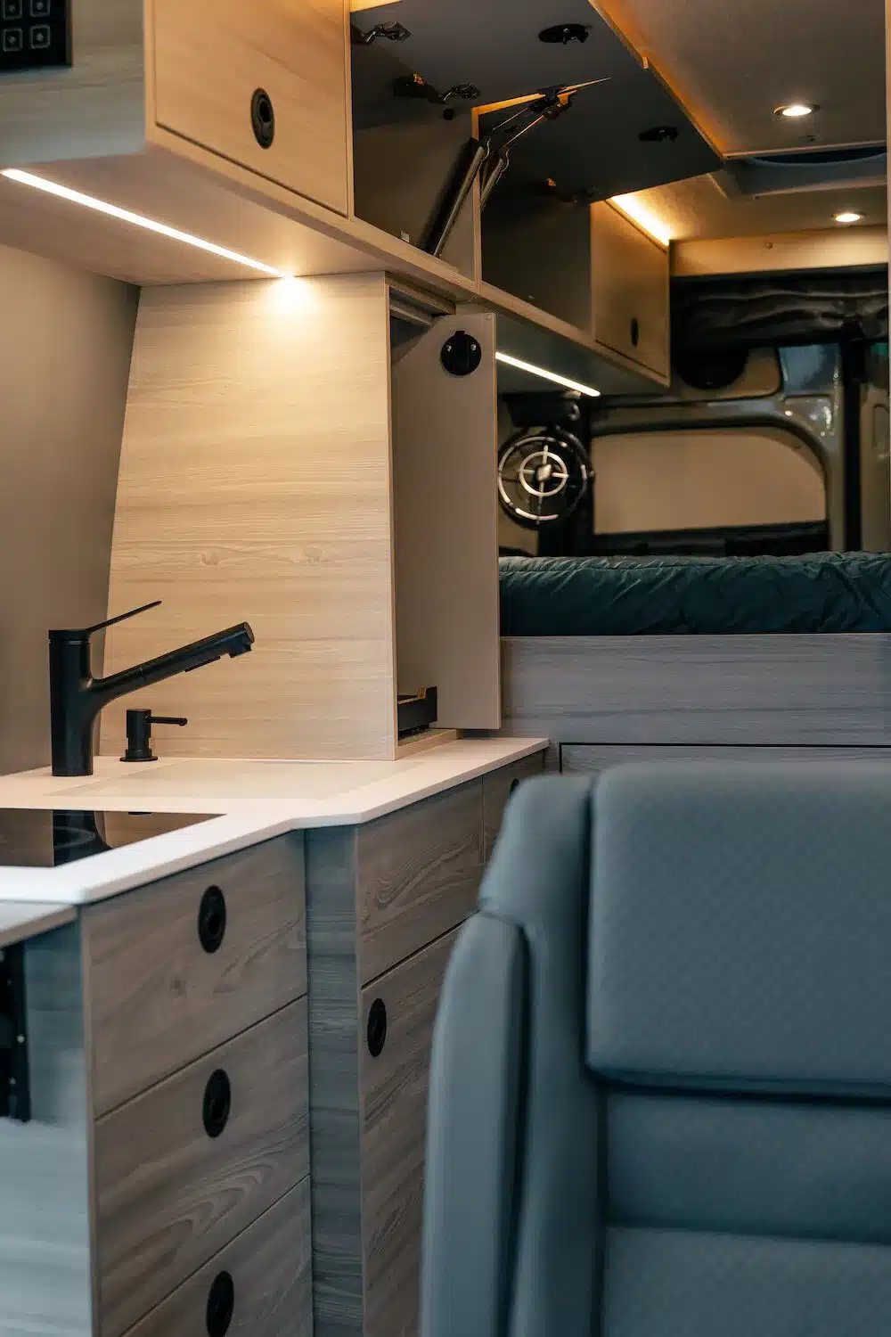 Moderne Küchenzeile und Stauraum im Innenraum eines ausgebauten Campervans mit hellem Holzdekor und schwarzer Armatur