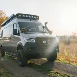 Benchmark Vehicles Green Lantern Campervan auf einem Feldweg bei Sonnenaufgang, umgeben von herbstlichen Bäumen.