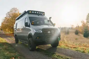 Benchmark Vehicles Green Lantern Campervan auf einem Feldweg bei Sonnenaufgang, umgeben von herbstlichen Bäumen.