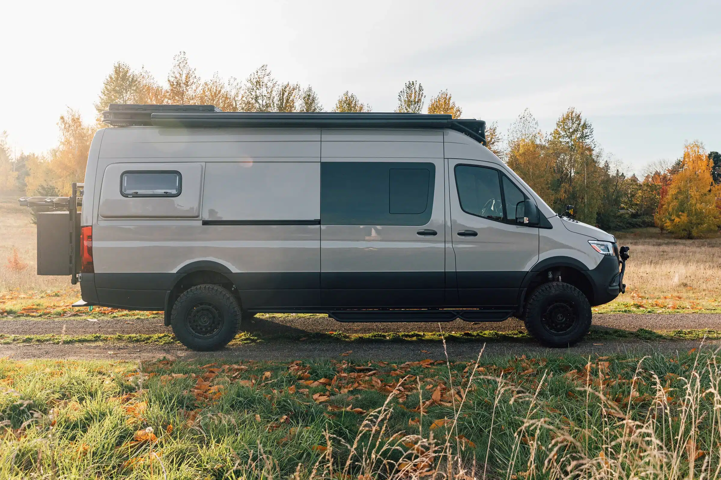 Seitenansicht des Benchmark Vehicles Green Lantern Campervans auf einem Feldweg, umgeben von herbstlicher Natur