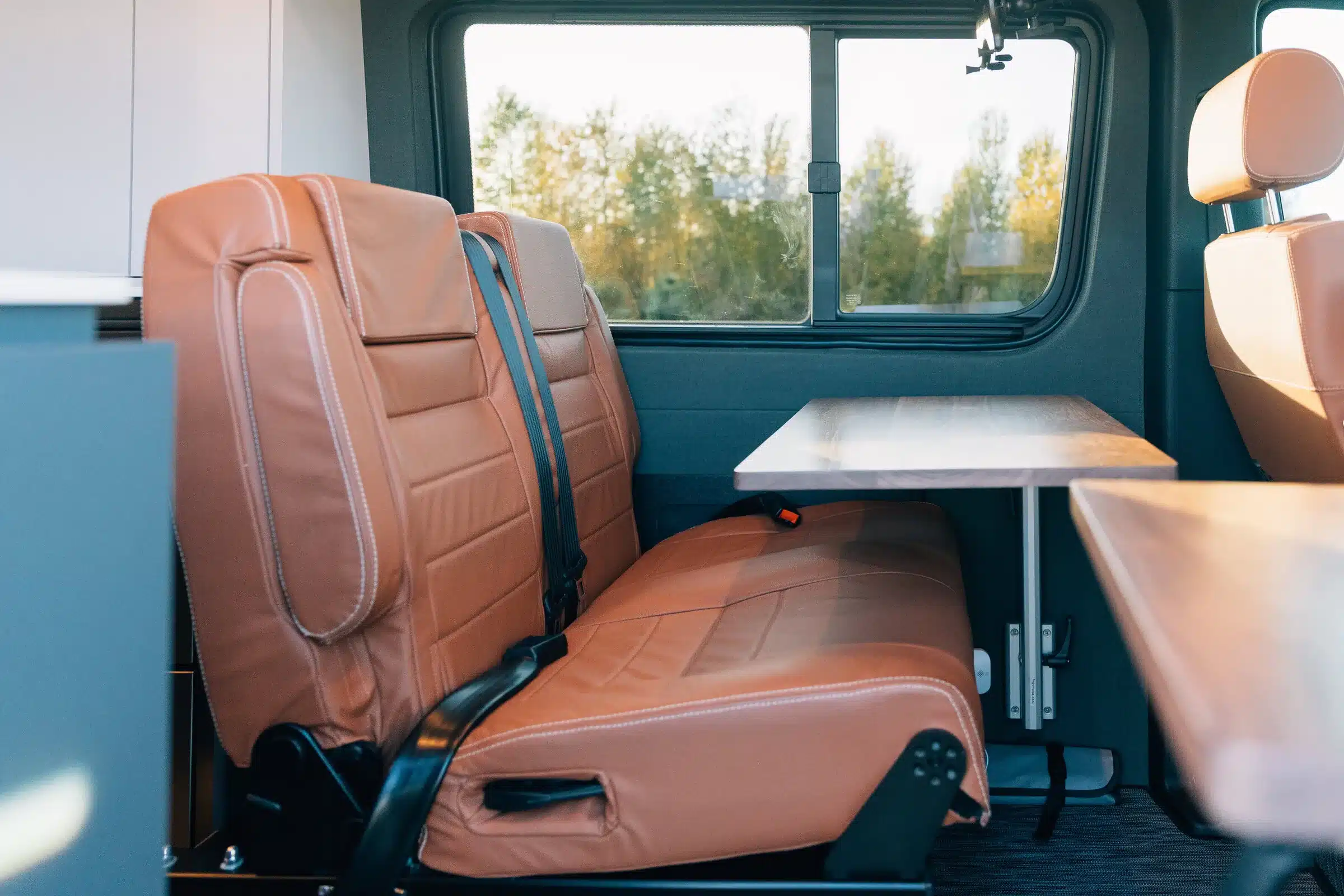 Sitzbank mit braunen Polstern und Tisch im Innenraum eines Benchmark Vehicles Green Lantern Campervans