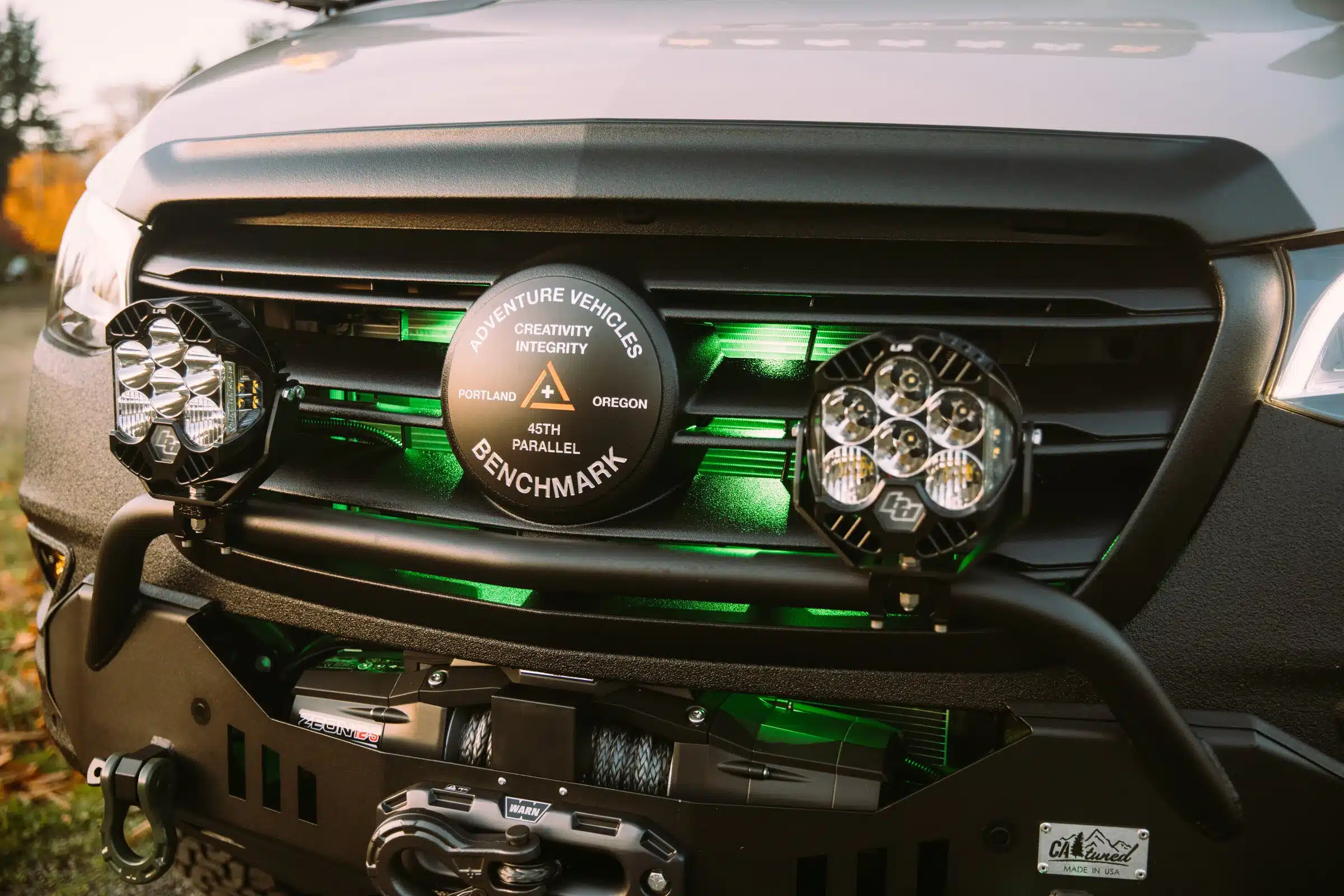 Nahaufnahme des Frontgrills eines Benchmark Vehicles Green Lantern Campervans mit Zusatzscheinwerfern, Seilwinde und grünem Licht