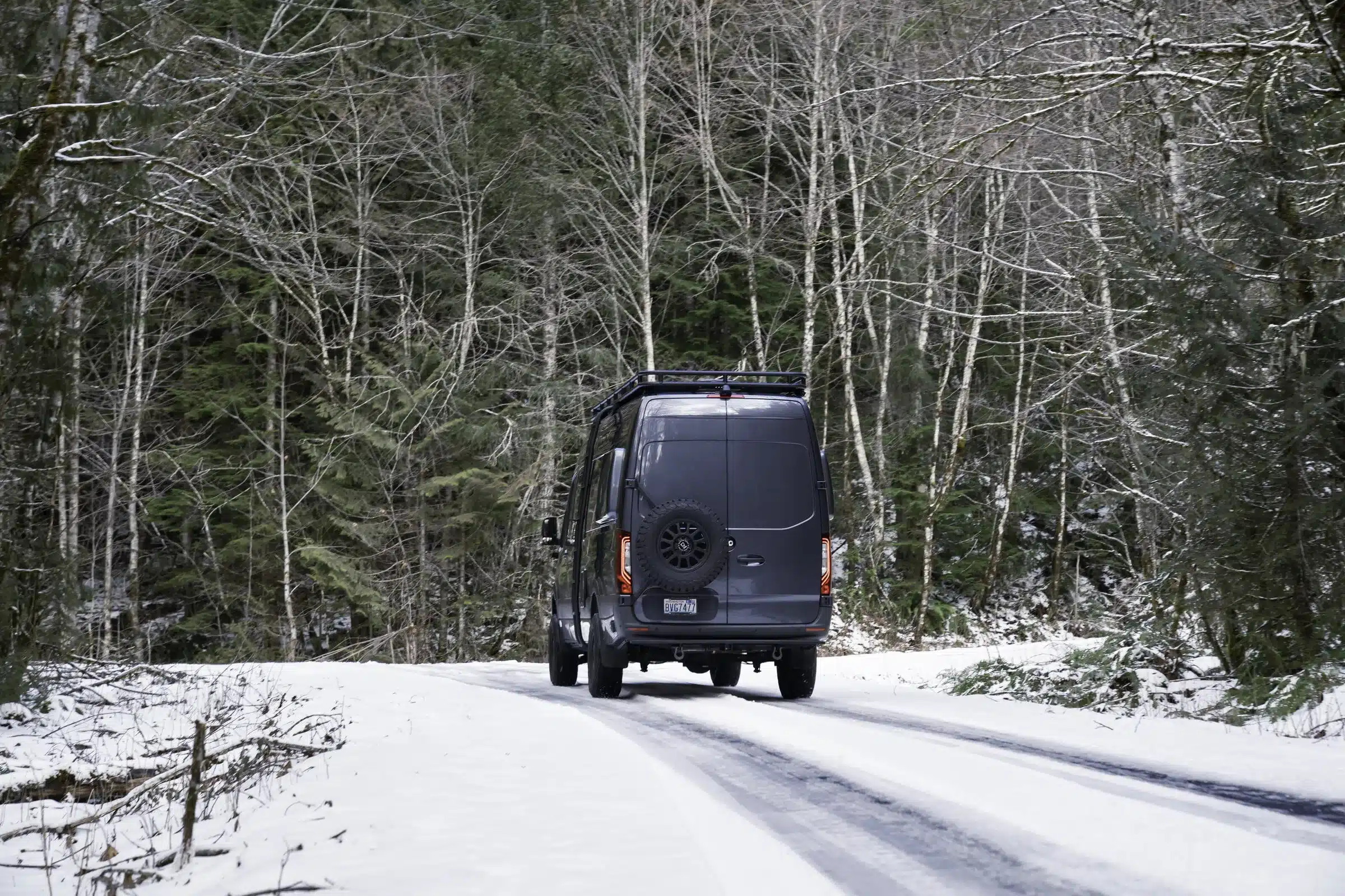 Benchmark Vehicles Lolo Mercedes Sprinter 170 4x4 fährt auf verschneiter Straße durch einen winterlichen Wald
