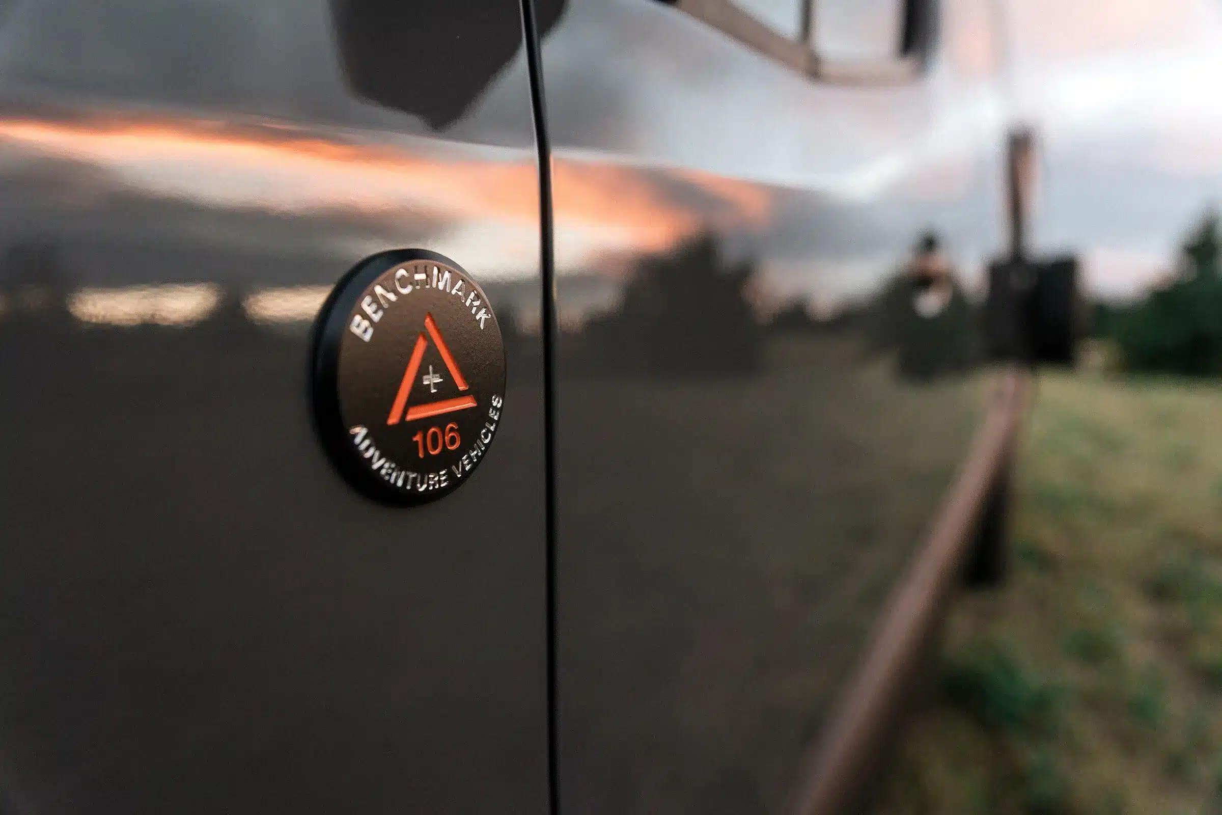 Detailaufnahme des Benchmark Adventure Vehicles Emblems an der Fahrzeugseite des Salathé Kastenwagens bei Sonnenuntergang