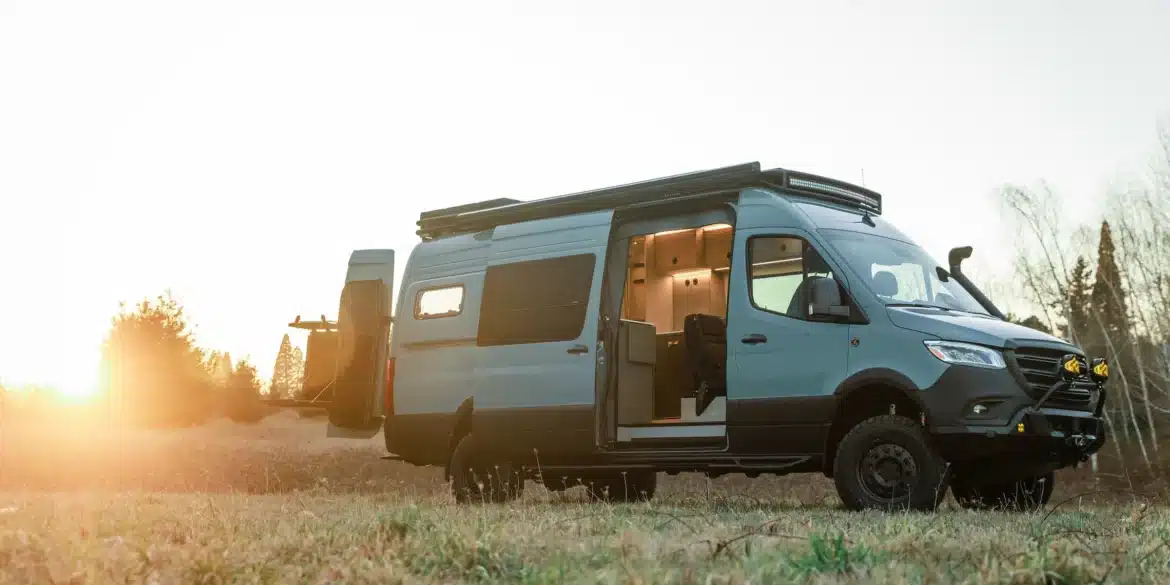 Benchmark Vehicles Strider Offroad-Campervan mit geöffneter Tür auf einer Wiese im Sonnenuntergang