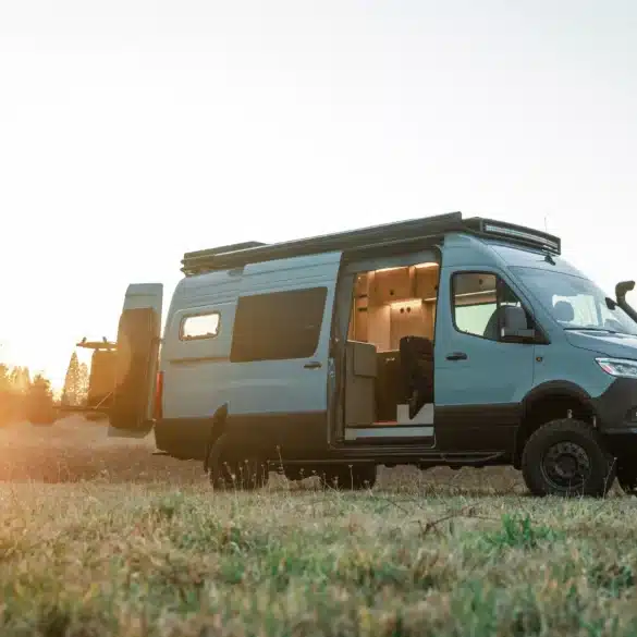 Benchmark Vehicles Strider Offroad-Campervan mit geöffneter Tür auf einer Wiese im Sonnenuntergang