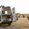 Heckansicht eines ausgebauten Kastenwagens The Grit mit geöffneten Türen, großem Stauraum und fest installiertem Doppelbett, auf einem Feldweg stehend