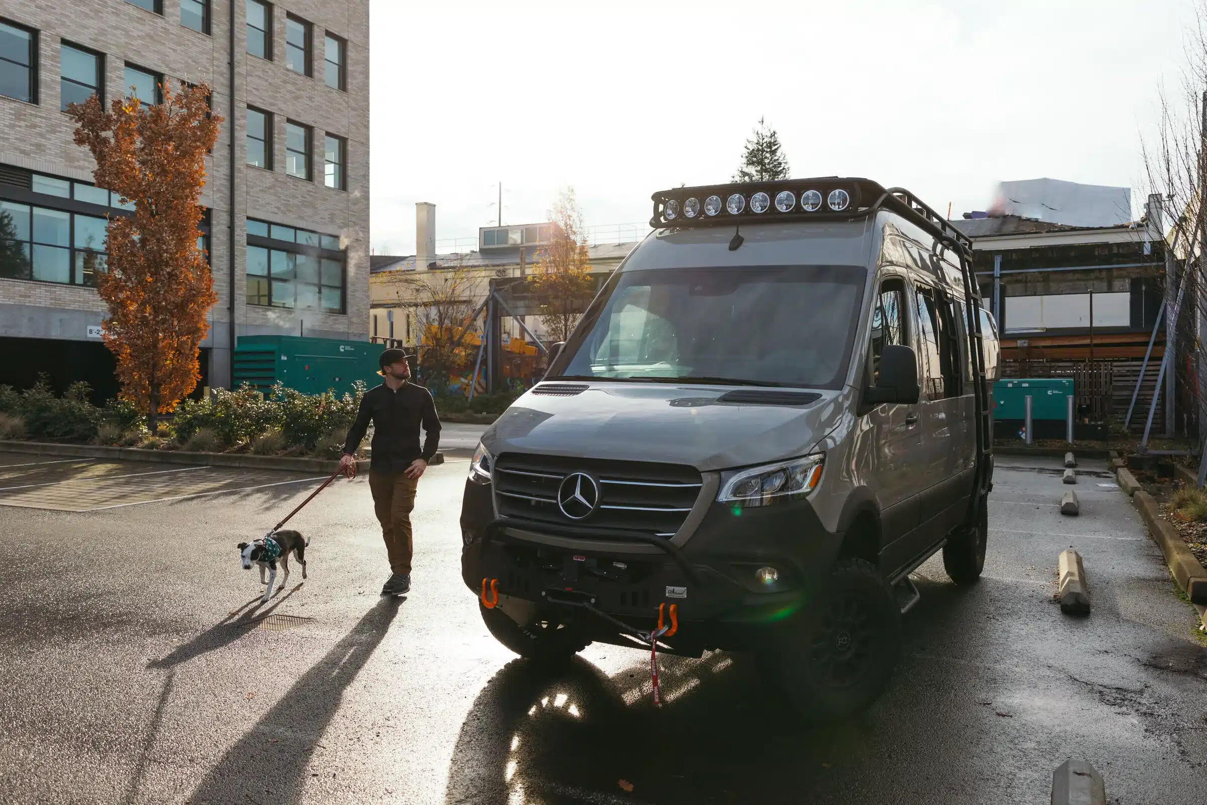 Ein Benchmark Zodiac Expeditionsvan auf Mercedes-Basis steht auf einem Parkplatz, im Vordergrund ein Mann mit Hund an der Leine